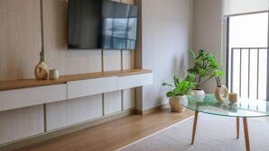 Un salon moderne avec un téléviseur fixé au mur, des étagères en bois, une table basse en verre et des plantes en pot.