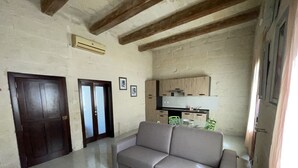 A living room with a sofa, a glass coffee table, and a kitchen area with cabinets and a countertop.