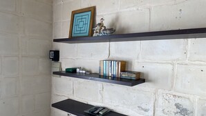 A room with a brick wall, three black shelves, a framed picture, and a small bird figurine.