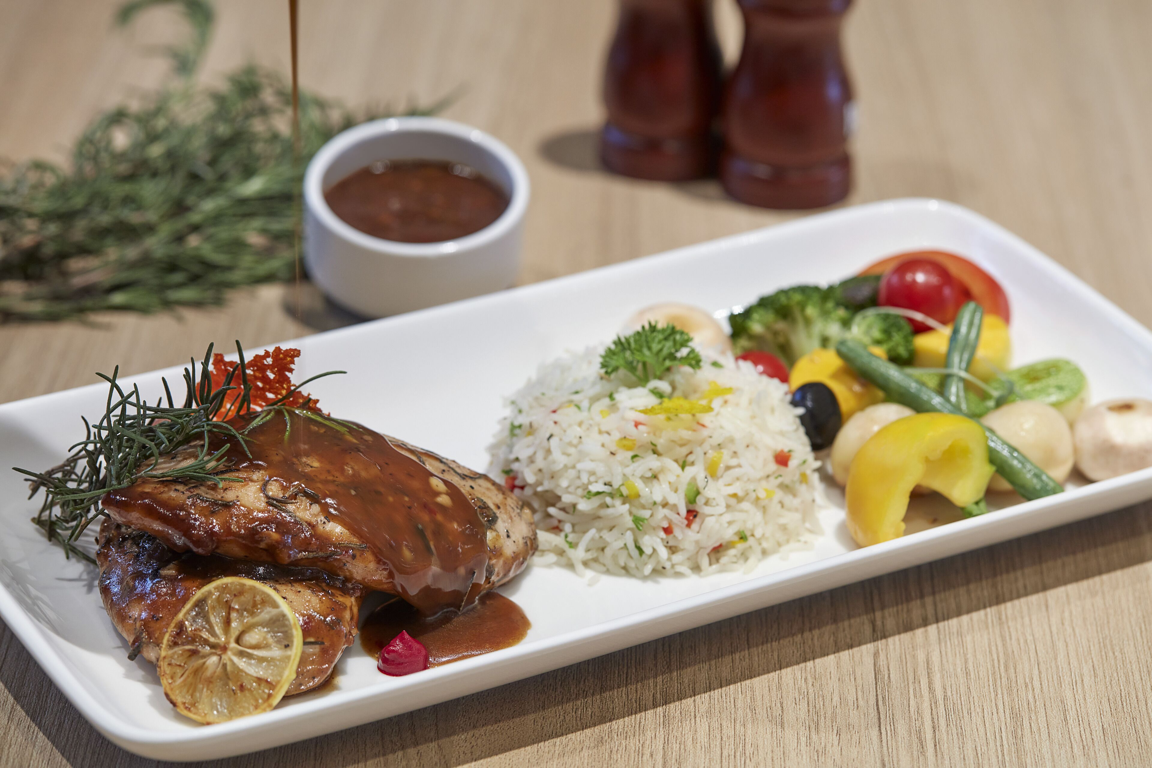 Une assiette rectangulaire blanche contenant de la viande grillée, du riz et des légumes.