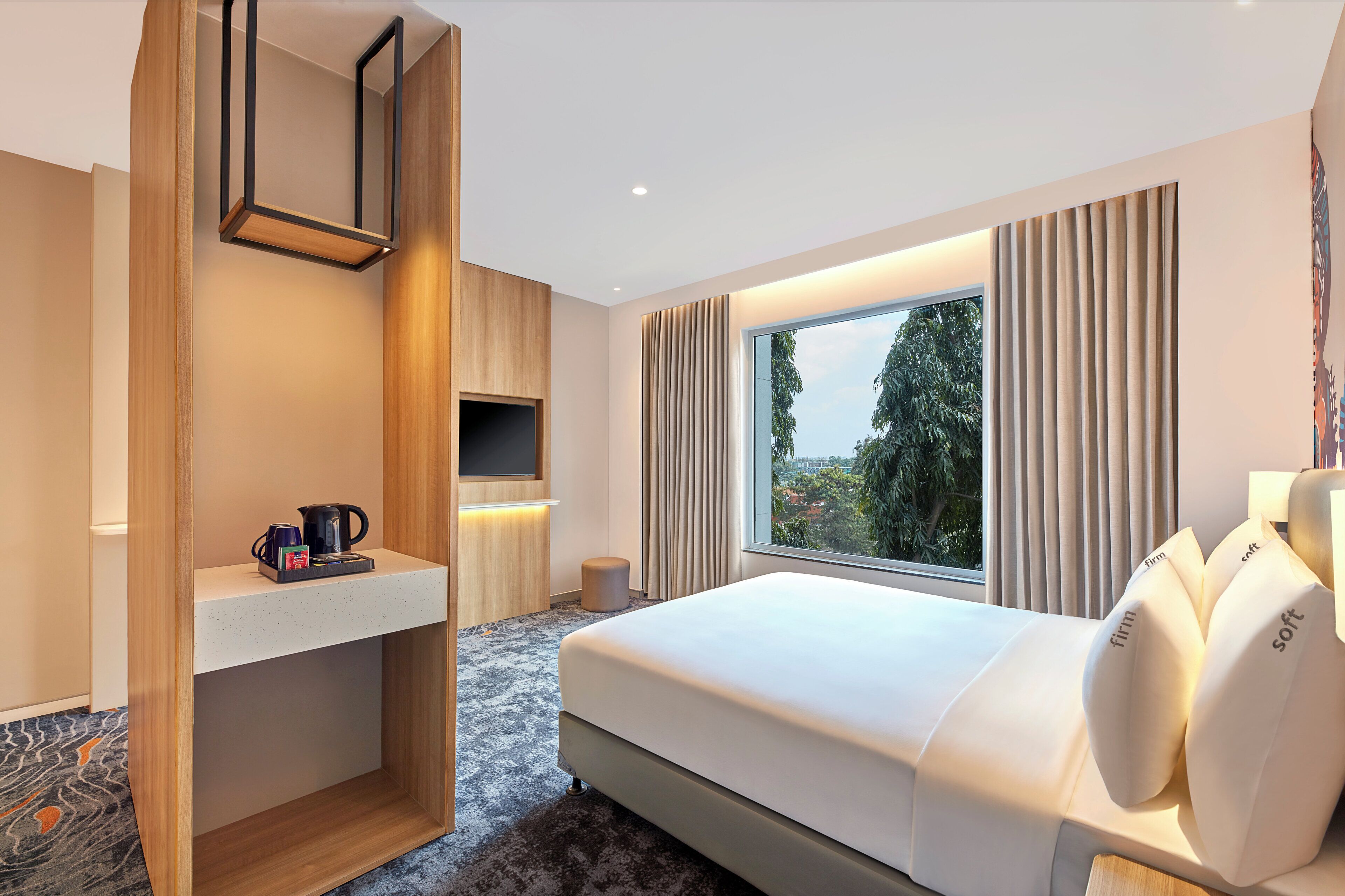 Habitación de hotel moderna con una cama grande, televisión, cafetera y vistas a árboles desde la ventana.