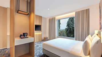 Habitación de hotel moderna con una cama grande, televisión, cafetera y vistas a árboles desde la ventana.