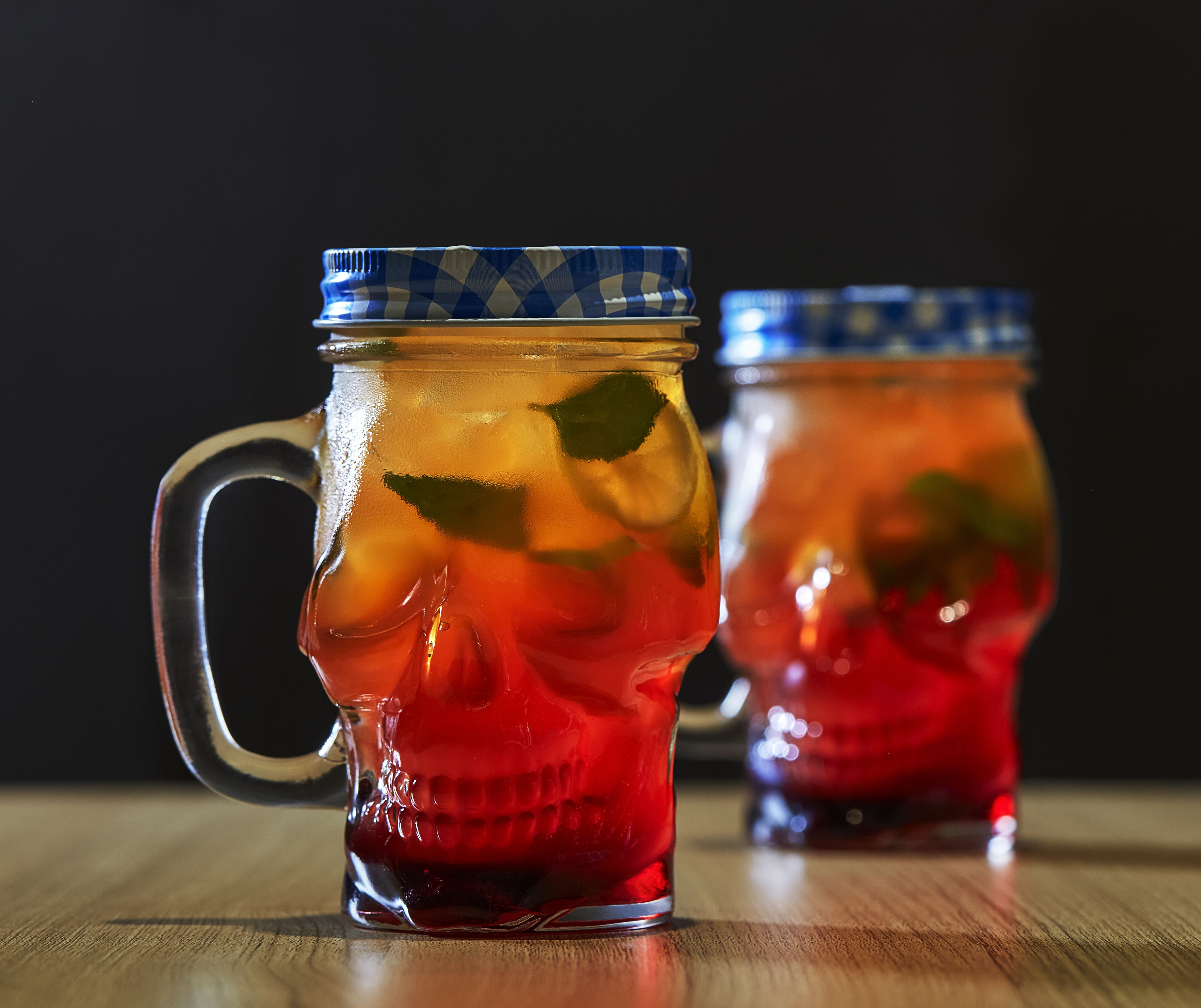 Two glass mugs with handles, filled with a red liquid and mint leaves, placed on a wooden surface.