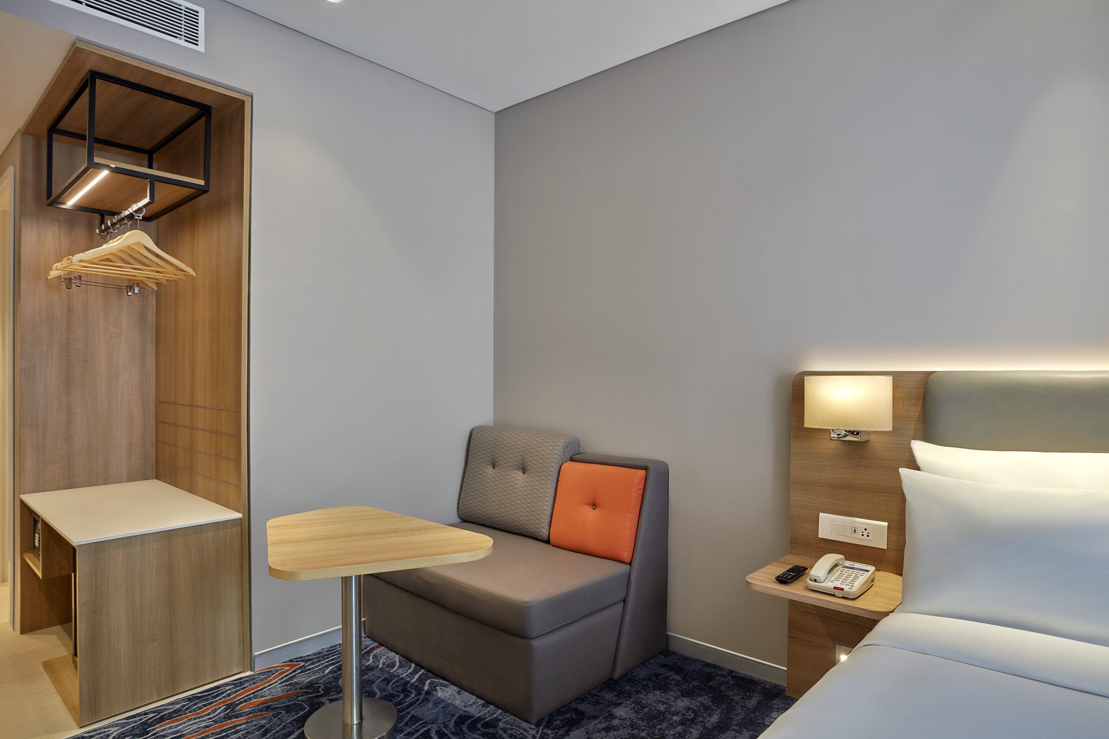 Een knus hotelkamer met een slaapbank, een klein tafeltje, een nachtkastje met lamp en een telefoon.