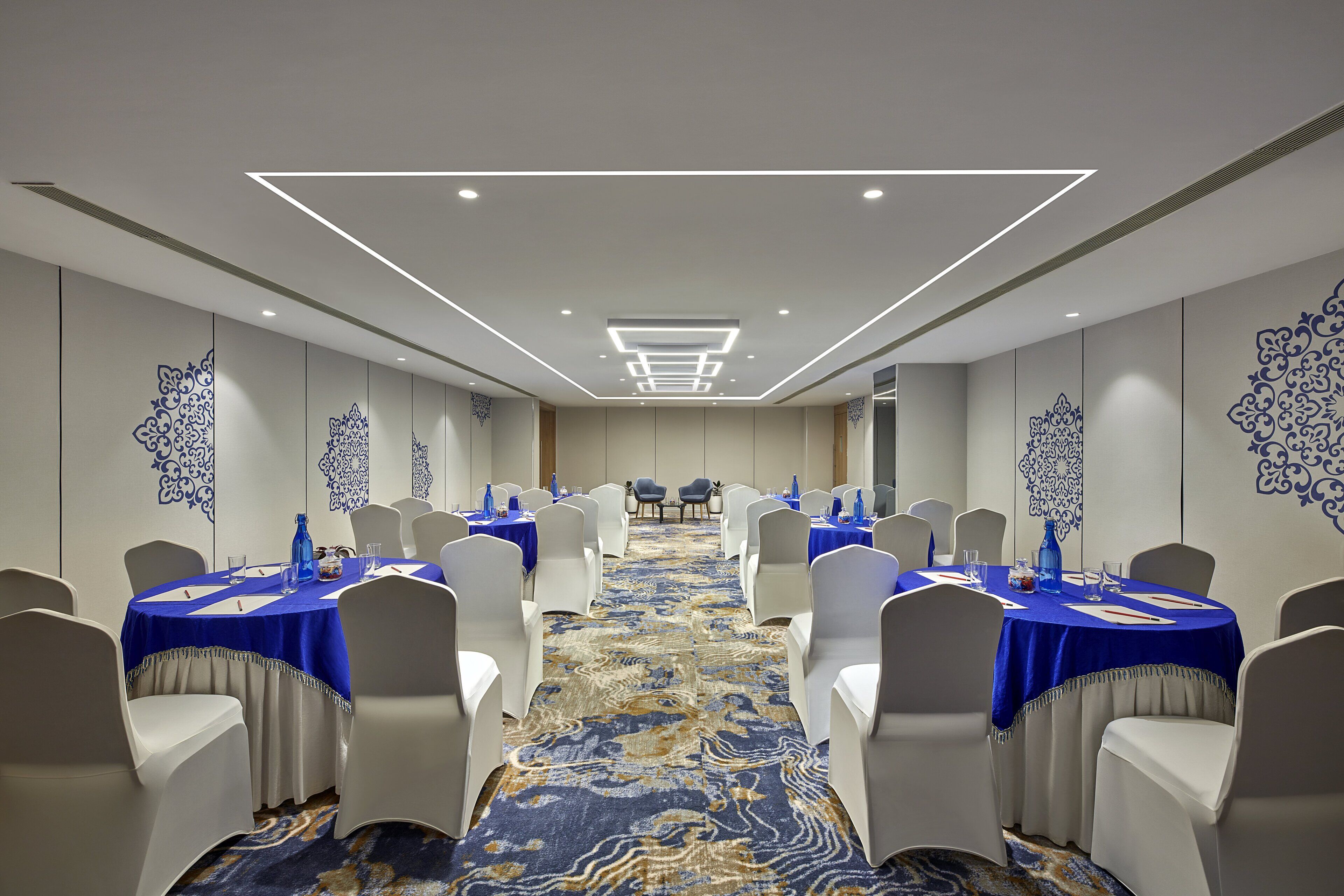 A conference room with round tables, white chairs, and blue tablecloths.