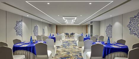 A conference room with round tables, white chairs, and blue tablecloths.