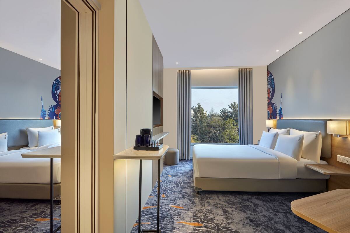 A hotel room with two beds, a small table, a chair, and a large window with curtains.