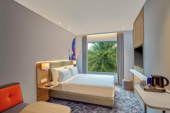 Habitación de hotel con cama, mesita de noche, lámpara y vistas a palmeras a través de la ventana.