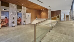 Een moderne lobby met marmeren vloeren, houten lambrisering en een glazen balustrade op de trap.