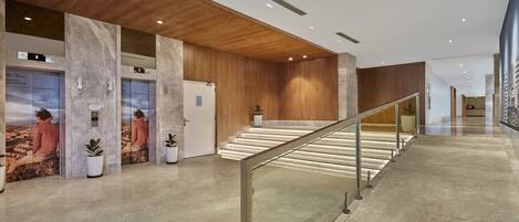 Een moderne lobby met marmeren vloeren, houten lambrisering en een glazen balustrade op de trap.