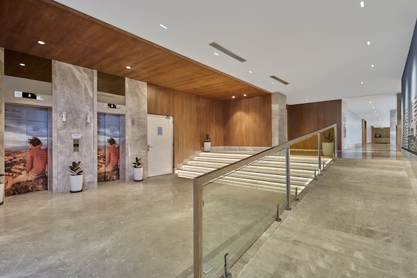 A modern lobby with marble floors, wooden paneling, a glass railing, and potted plants.