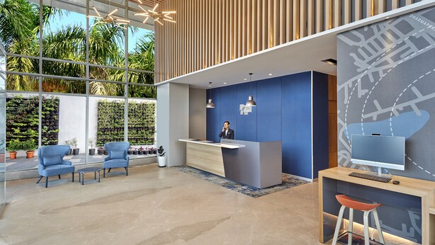 Een modern receptiegebied met een houten receptiebalie, blauwe wanden en een groot raam met uitzicht op groen.