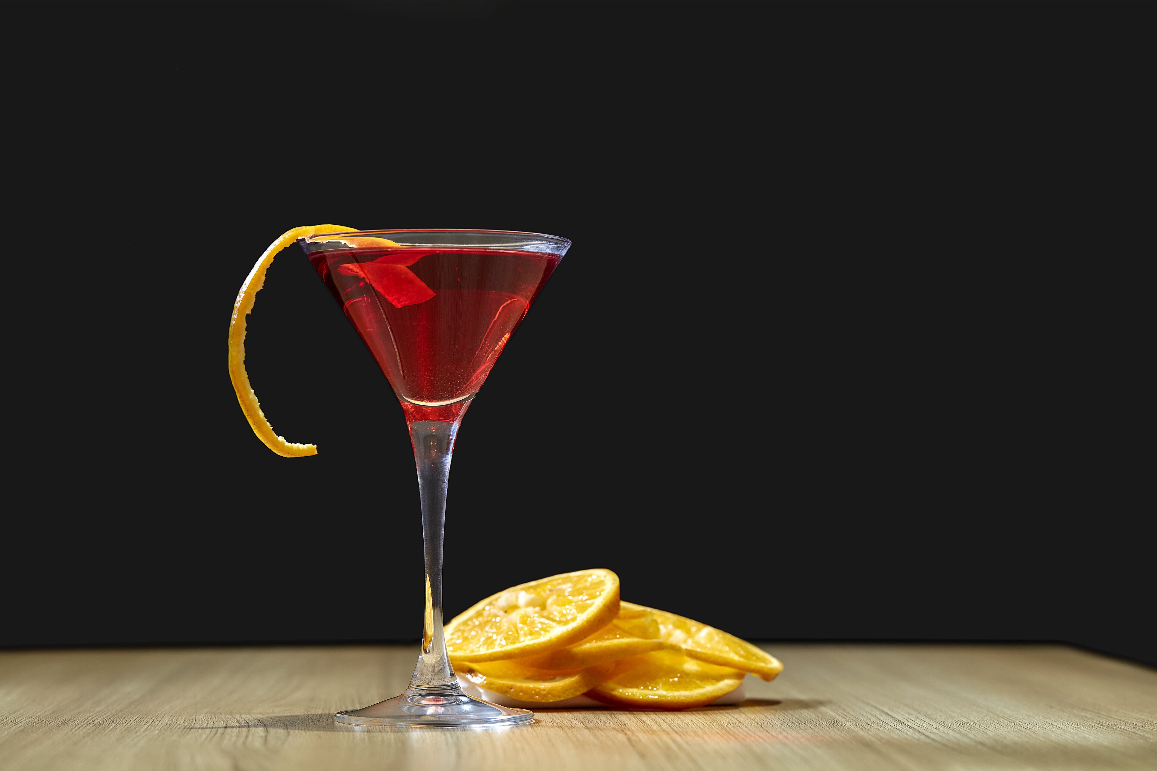 A martini glass with a lemon garnish on a wooden surface against a dark background.