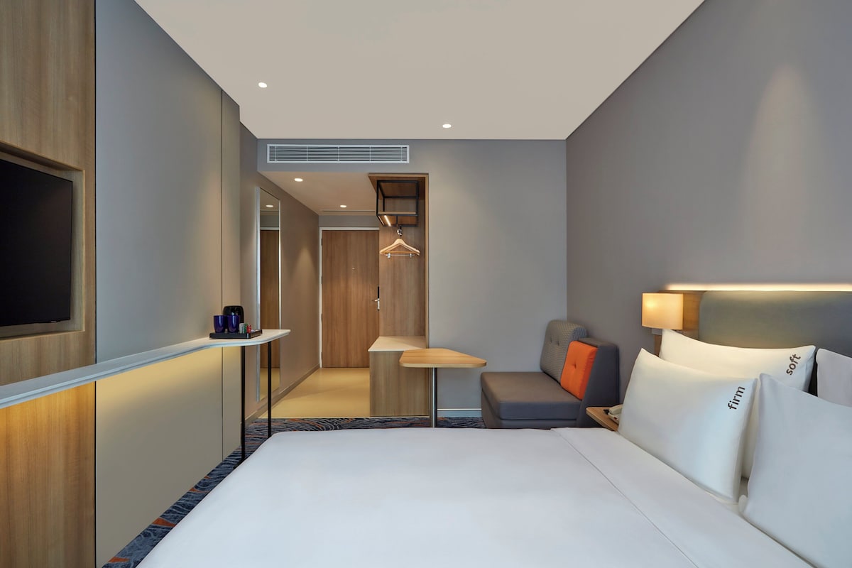 Ett modernt hotellrum med en stor säng, ett sängbord, en hängande lampa, en soffa och en tv.