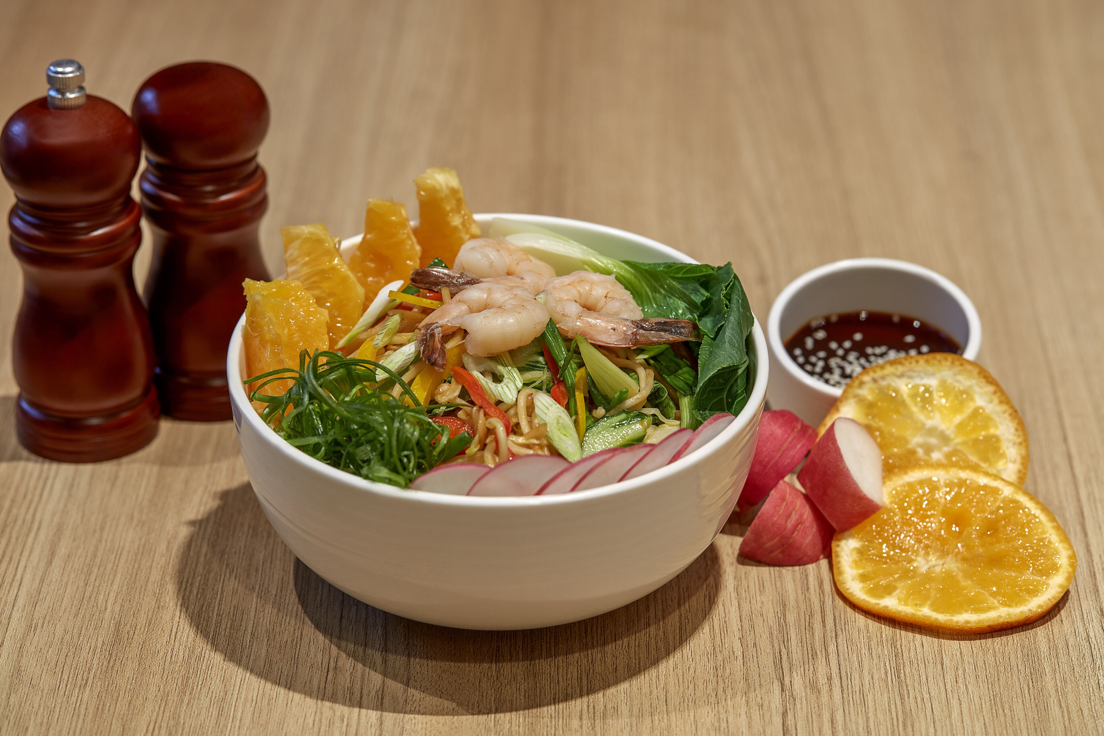 Un tazón de ensalada con camarones, verduras y gajos de naranja sobre una mesa de madera.