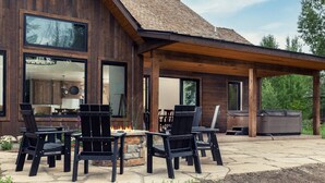 A modern wooden house with a covered patio area featuring outdoor furniture and a fire pit. - Redtail Rendezvous with Hot Tub (Driggs)