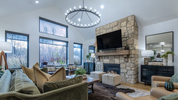 A modern living room with a stone fireplace, large windows, and a flat-screen TV. - Redtail Rendezvous with Hot Tub (Driggs)