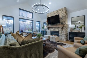 Un salon moderne avec une cheminée en pierre, de grandes fenêtres et un téléviseur à écran plat.