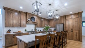 A modern kitchen with wooden cabinets, a central island with chairs, stainless steel appliances, and pendant lighting. - Redtail Rendezvous with Hot Tub (Driggs)