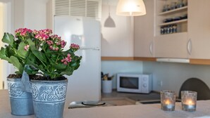 A modern kitchen with a white refrigerator, a microwave, and a hanging pendant light. There are two potted plants with pink flowers on the counter. - "Line" - 10m from the sea by Interhome (Glesborg)