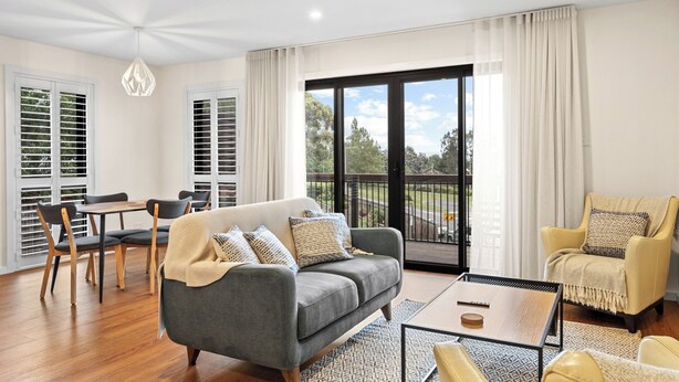 A modern living room with a grey sofa, a yellow armchair, a coffee table, and a dining area with a table and chairs. - Architectural Home: Near Gorge with Tamar Views (Launceston)