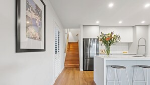 A modern kitchen with a stainless steel refrigerator, wooden flooring, white cabinetry, and a bar area with stools. - Architectural Home: Near Gorge with Tamar Views (Launceston)