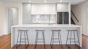 A modern kitchen with white cabinets, a stainless steel refrigerator, and three wooden stools. - Architectural Home: Near Gorge with Tamar Views (Launceston)