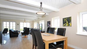 Un vaste espace dédié à la salle à manger, avec une table en bois et des chaises noires, de grandes fenêtres et un plafond haut avec des poutres apparentes.