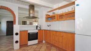 Une cuisine équipée d’une cuisinière, d’un four et d’un réfrigérateur blanc. On y trouve un meuble en bois avec des portes en verre et une arche en briques.