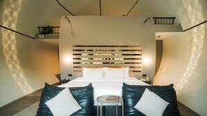 Ein modernes Hotelzimmer mit einem großen Bett, zwei Ledersofas, einem kleinen Tisch und einem dekorativen Kopfteil.