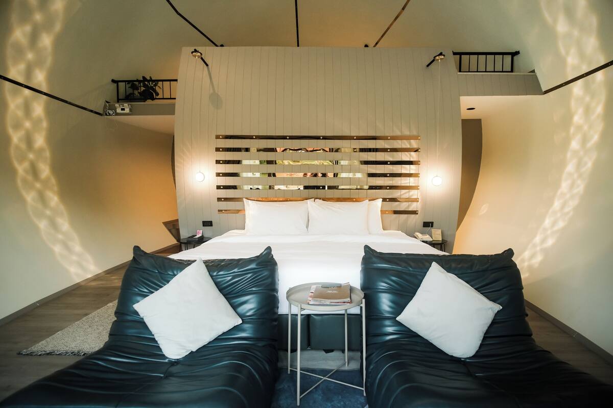 Een moderne hotelkamer met een groot bed, twee leren banken, een kleine tafel en een decoratief hoofdeinde.