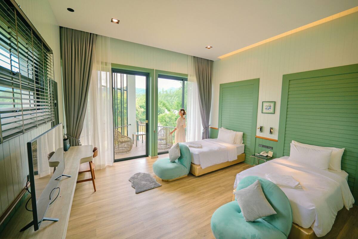 Een moderne hotelkamer met een groot bed, een bureau en een balkon met uitzicht op groen.