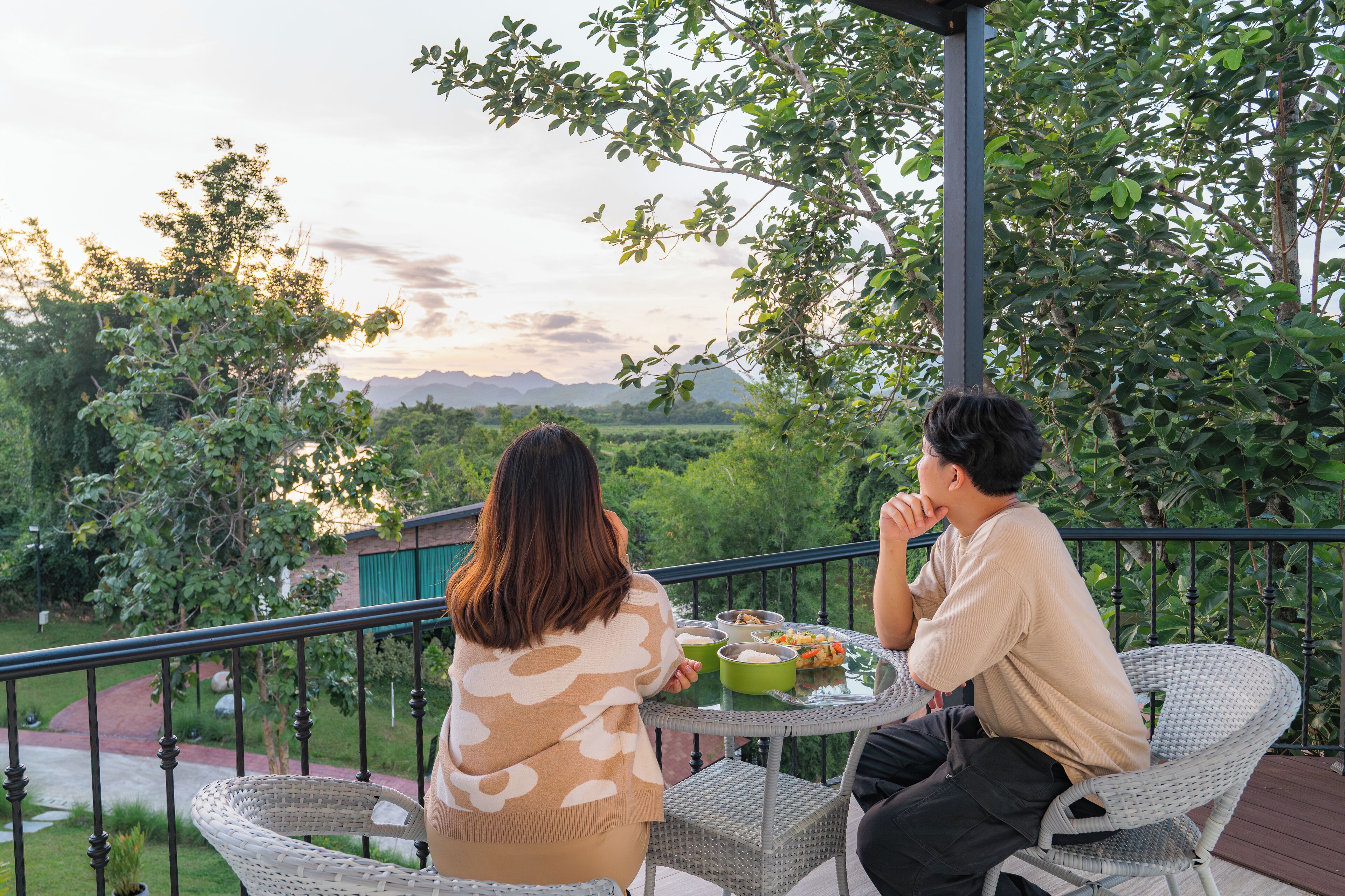 A couple dining at an outdoor table with a view of a lush garden and mountains in the background.