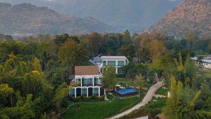 Ein modernes Haus mit Swimmingpool, umgeben von üppiger Vegetation und Bergen im Hintergrund.