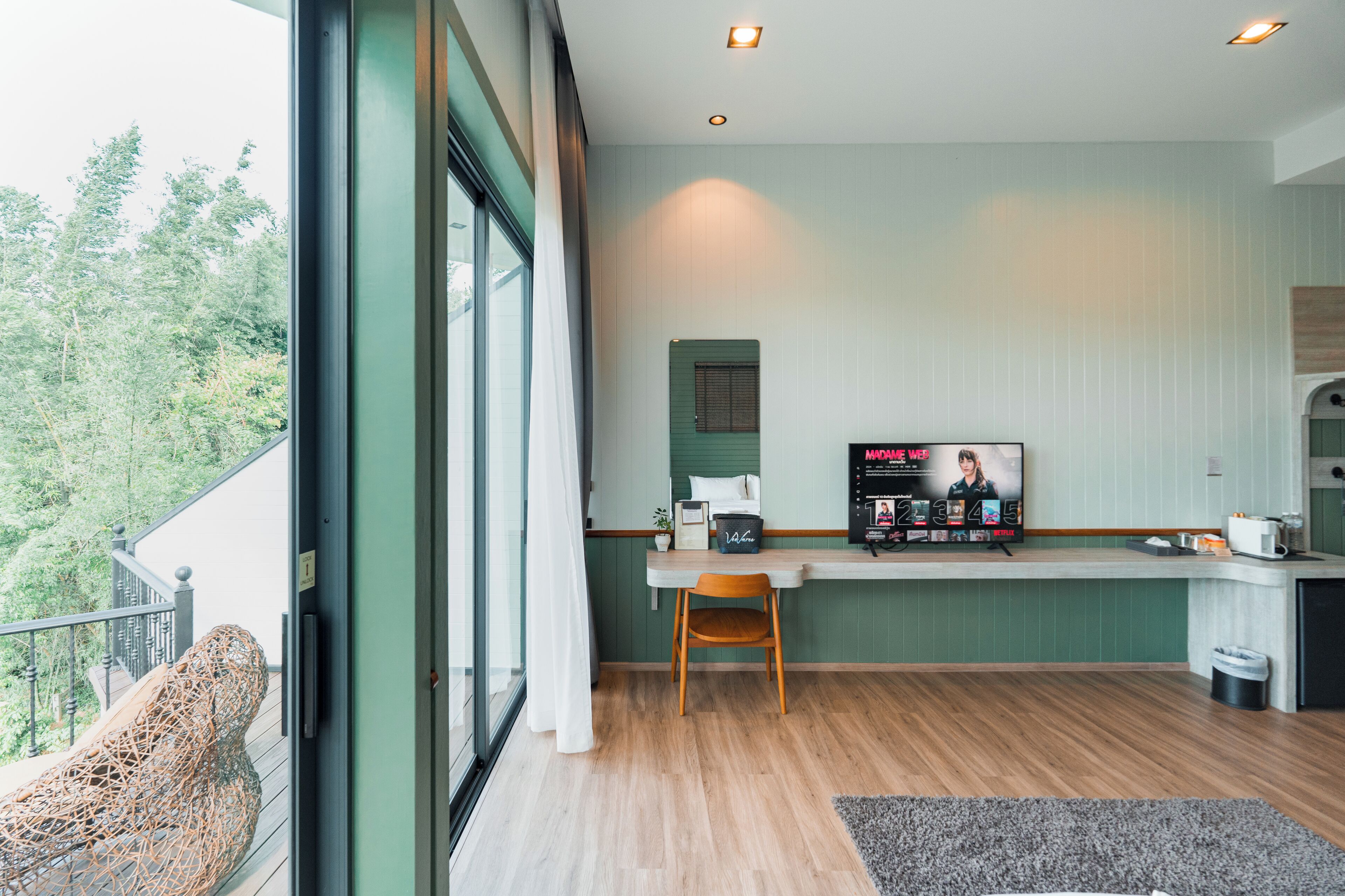 A modern kitchen with a wooden dining table, a TV, and a window overlooking greenery.
