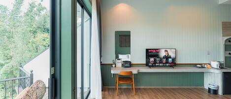 A modern kitchen with a wooden dining table, a TV, and a window overlooking greenery.