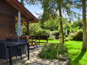 Une terrasse en bois avec des meubles d’extérieur, un espace salon couvert et un jardin luxuriant.