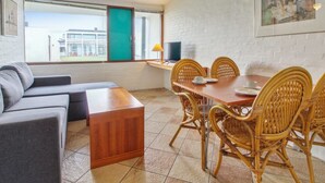 Ein modernes Wohnzimmer mit einer Couch, einem Holztisch, einem Esstisch mit Korbstühlen, einem Fernseher und einem Gemälde an der Wand.