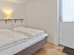 Een bed met witte lakens in een kamer met witte muren en een deur.