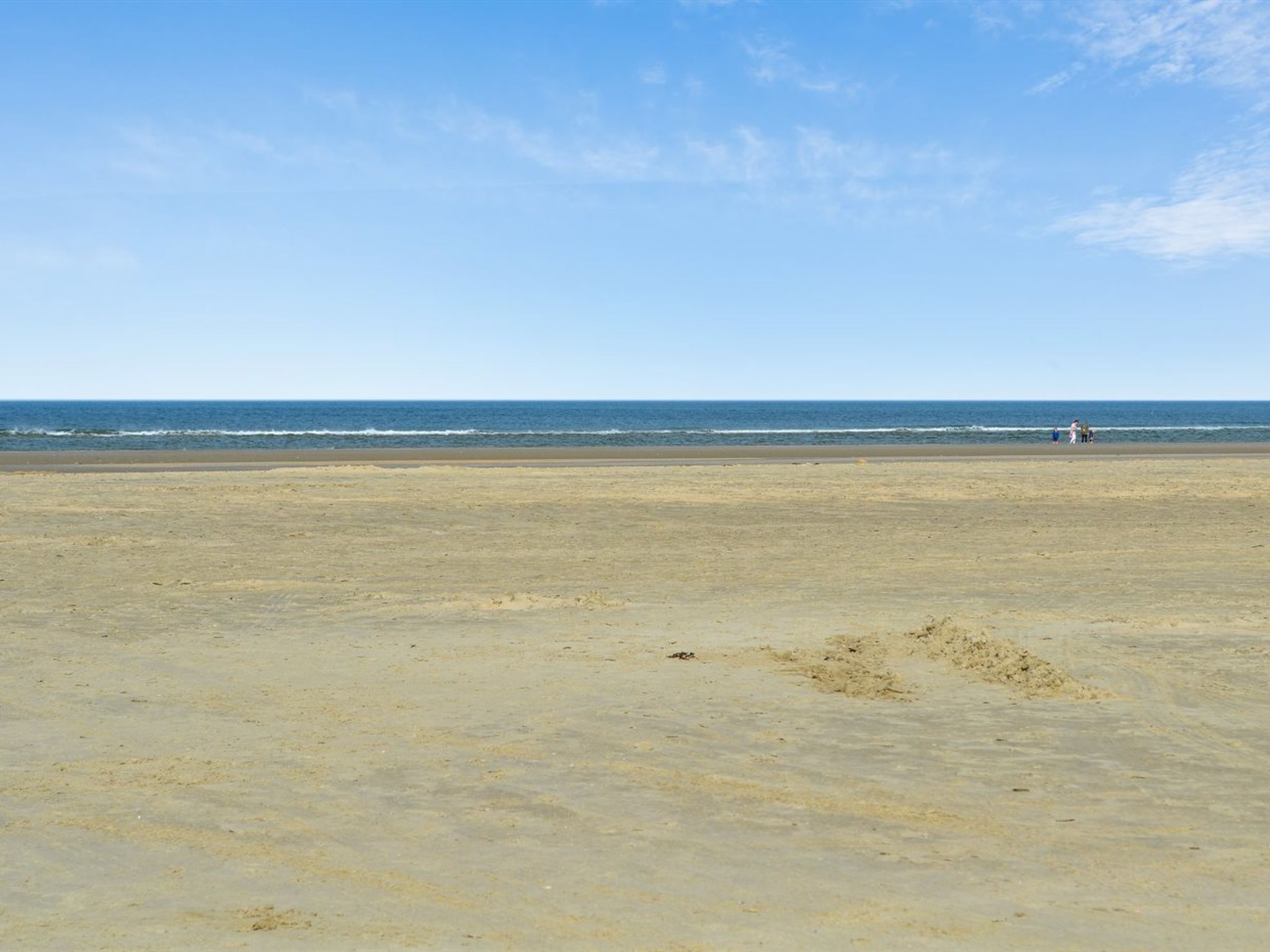 Ein weiter Sandstrand mit blauem Himmel und ruhiger See.
