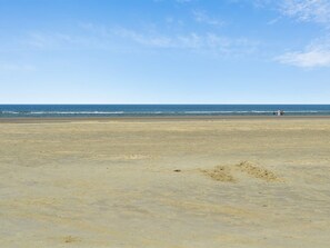 En bred sandstrand med klar himmel och stilla hav.