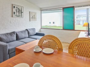 Een moderne kamer met een grijze bank, een houten eettafel met stoelen en kunstwerken aan de wanden.