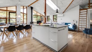 Een ruime keuken met een centraal eiland, grote ramen en een eetgedeelte met houten stoelen.