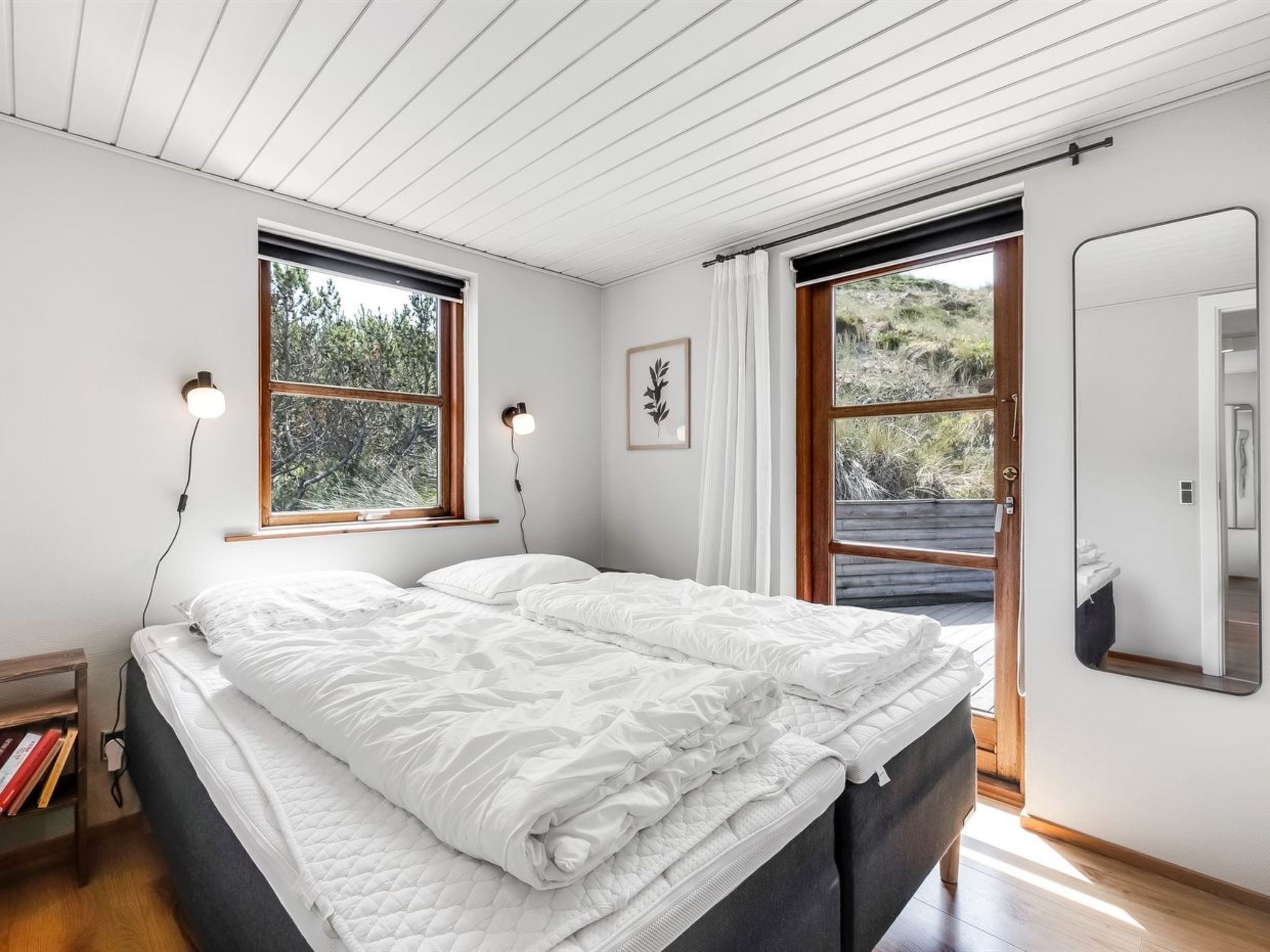 A bedroom with a bed, two windows, a door, and a mirror.