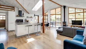 Een ruime woonkamer met een keuken, houten vloeren en grote ramen die veel natuurlijk licht binnenlaten.