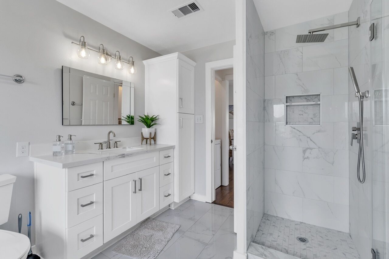 Un baño moderno con un tocador blanco, un espejo grande y una ducha a ras de suelo con puerta de cristal.