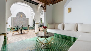 Une pièce avec un sol à motifs verts, des murs blancs, un canapé blanc et un coin repas comprenant des chaises et une table.