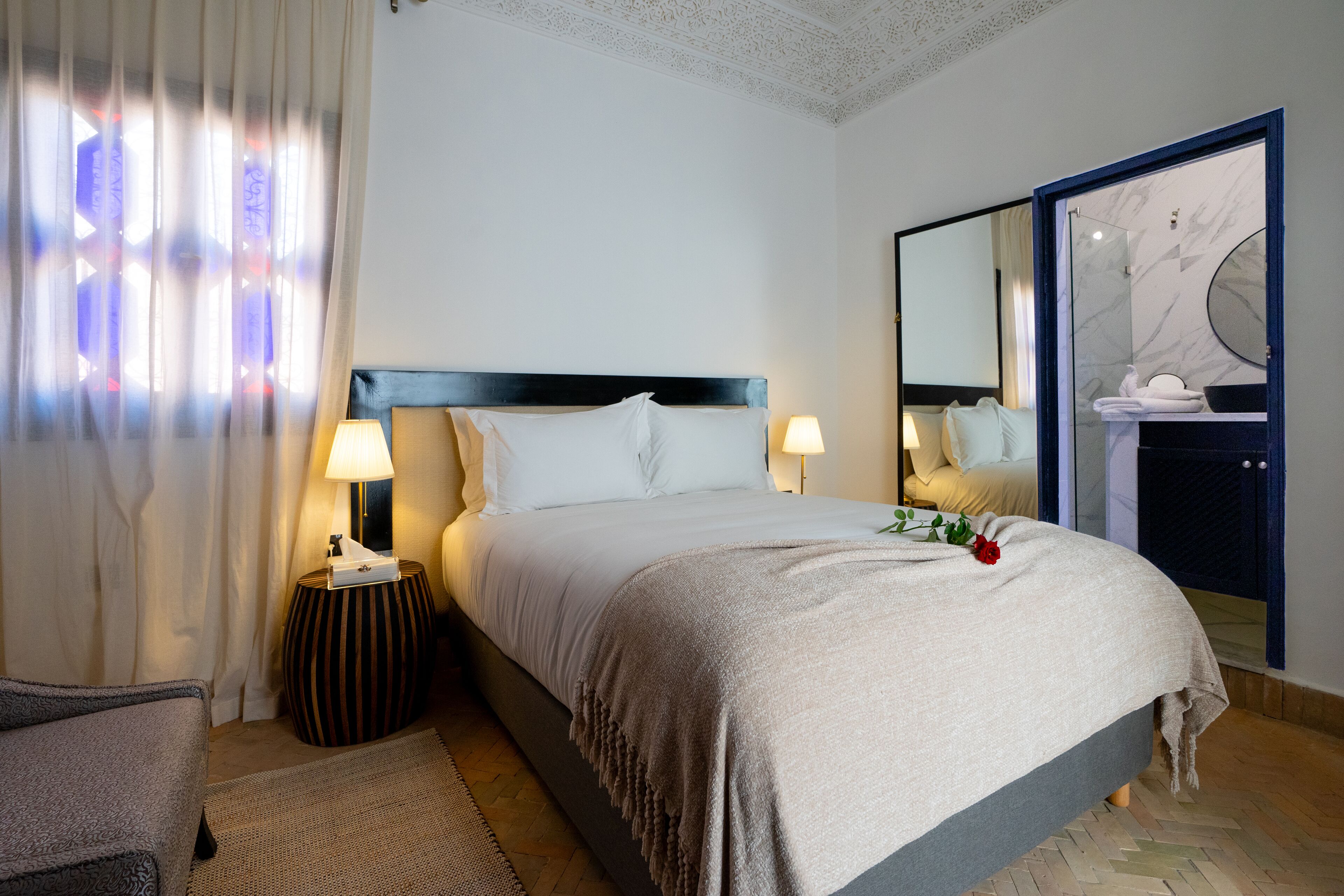 A neatly arranged hotel room with a bed, bedside lamps, a mirror, and a view of the bathroom.