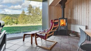 A cozy room with a large window, a wooden interior, a stone fireplace, and a comfortable chair. - "Merja" - 3km from the sea by Interhome (Ebeltoft)