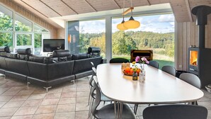 A modern living room with a large sofa, a dining table, and a TV. There is a fireplace and a large window overlooking a forested area. - "Merja" - 3km from the sea by Interhome (Ebeltoft)